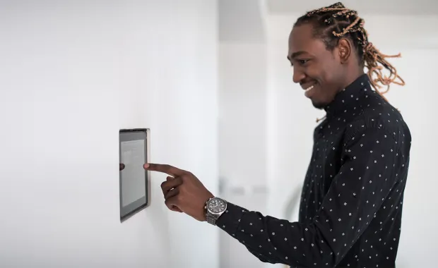 Man adjusting the temperature at home using a smart meter monitor against the wall