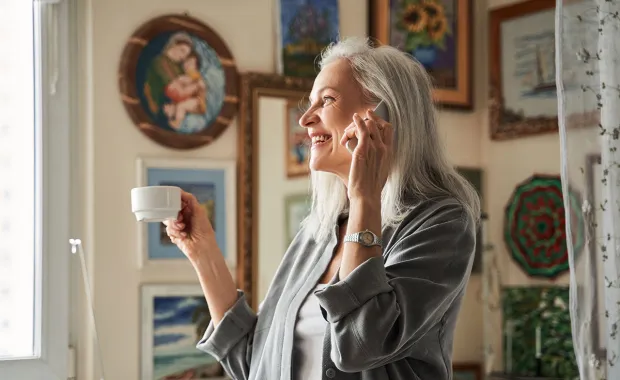 Smiling woman standing and talking on phone while holding cup