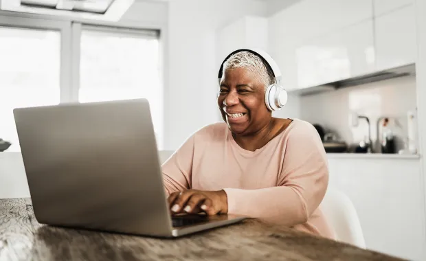 woman sitting in kitchen using laptop wearing white headphones