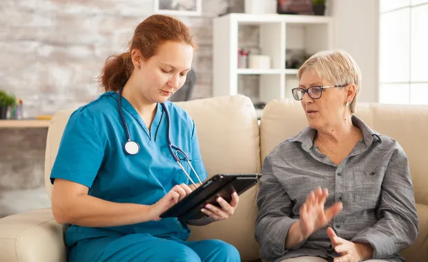 Nurse and patient sitting on a sofa discussing therapy using an ipad.