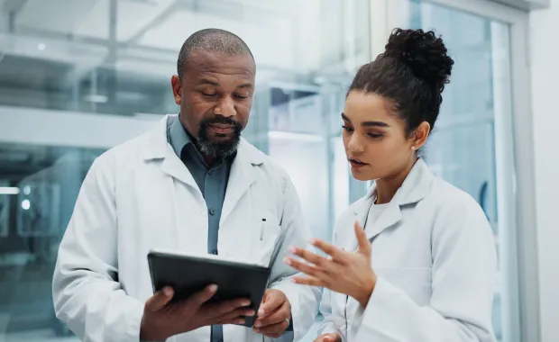 Two healthcare professionals in white coats review a tablet together in a bright, modern laboratory