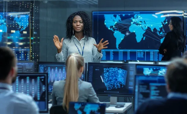 a woman speaking to colleagues in a control room