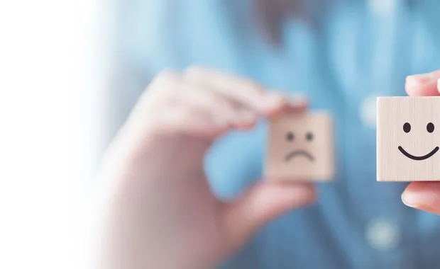Woman holding two wooden dice, one with a smiley face and one with a sad face