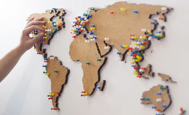 En kvinnlig hand sätter en nål på en anslagstavla i form av världskarta