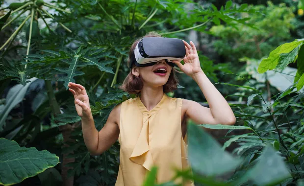 Frau inmitten von grünen Pflanzen im Gewächshaus mit VR (Virtual Reality) Brille