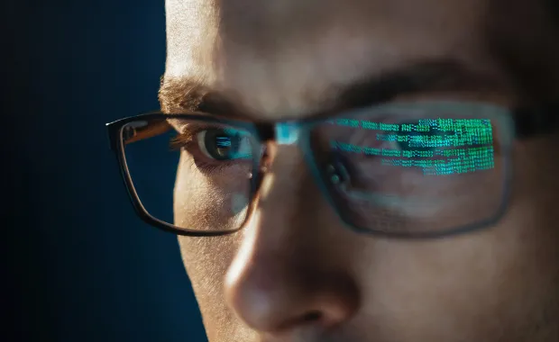 Nærbilde av mann med briller, grønn datakode reflektert i glassene.