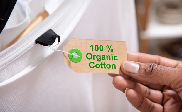 Hand som håller i en lapp med texten 100% organic cotton på en vit t-shirt