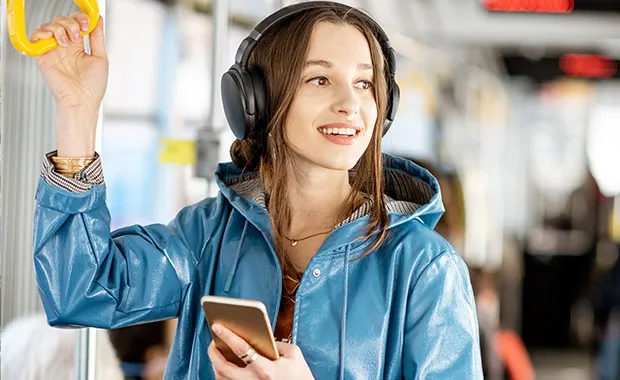 Kuvituskuva: Nuori matkustaja seisoo kuulokkeiden ja älypuhelimen kanssa modernissa raitiovaunussa