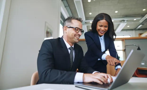 Manlig och kvinnlig kollega tittar leende på en laptop på kontoret