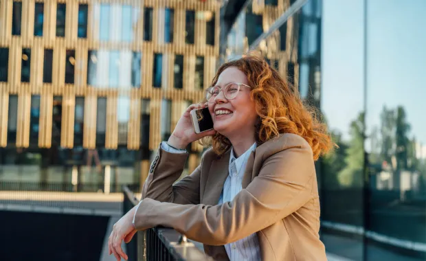 Glad affärskvinna som pratar i mobiltelefon framför kontorsbyggnad.