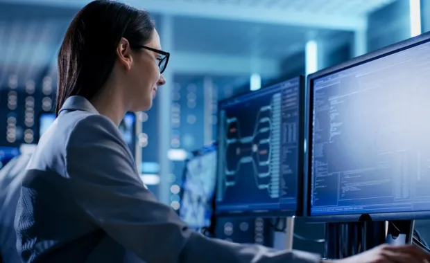 Softwareentwicklerin arbeitet an zwei Bildschirmen mit geöffnetem Programmcode.