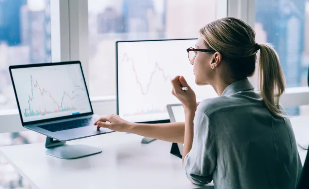 Woman reviews financial data on two monitors.
