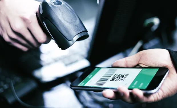 En person håller en smartphone med en QR-kod medan en annan skannar koden med en handscanner. Bilden visar en digital betalning i butiksmiljö.