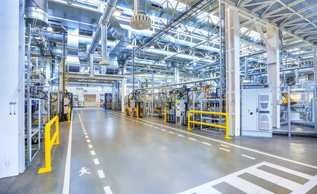 Interiör av en modern industrifabrik med produktionslinjer, rörsystem och teknisk utrustning. Gångvägar och säkerhetsmarkeringar syns i den ljusa och välorganiserade produktionsmiljön.