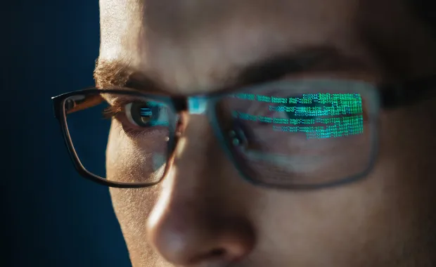 Nærbilde av mann med briller, grønn datakode reflektert i glassene.