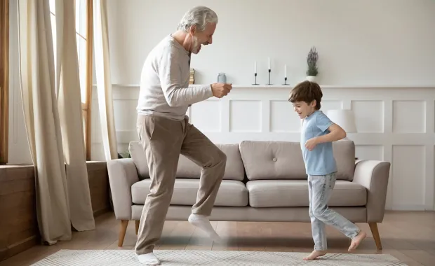 En äldre man och en pojke dansar tillsammans i vardagsrummet