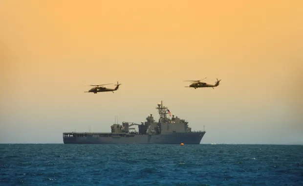 Helicopters hovering over a Navy battleship at sea