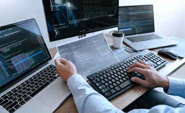 Mitu arvutit laual, programeerija töötab koodiga
