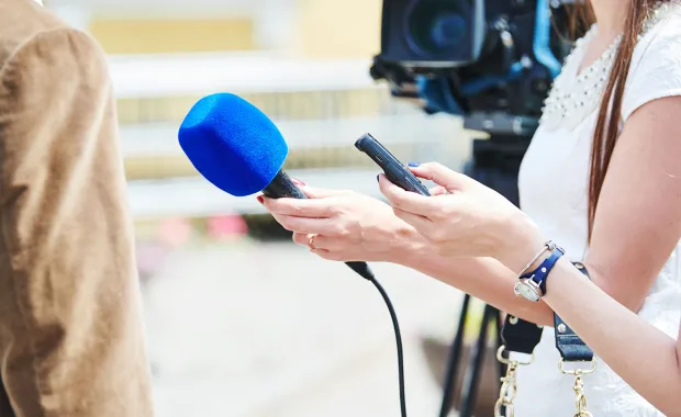 Eine Reporterin interviewt eine Person mit einem blauen Mikrofon