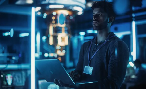 A researcher wearing an ID badge uses a laptop in a blue-lit laboratory