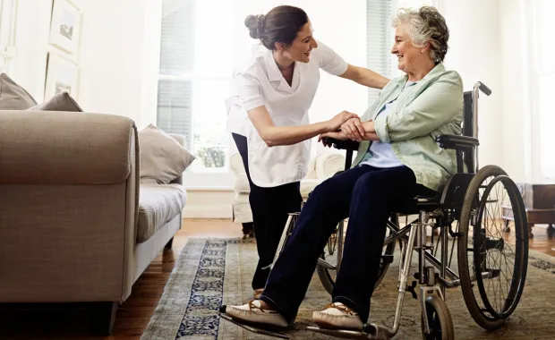 Kuvituskuva: sairaanhoitaja auttaa pyörätuolissa olevaa naista. 