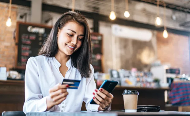 En dame på kafè som betaler med kredittkort over mobiltelefon