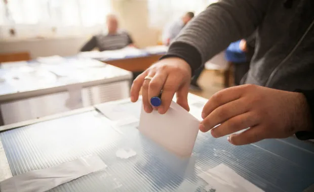 Eine Person wirft einen Wahlschein in eine Wahlurne