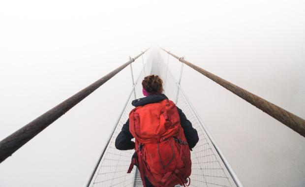 Person with backpack crossing suspended bridge