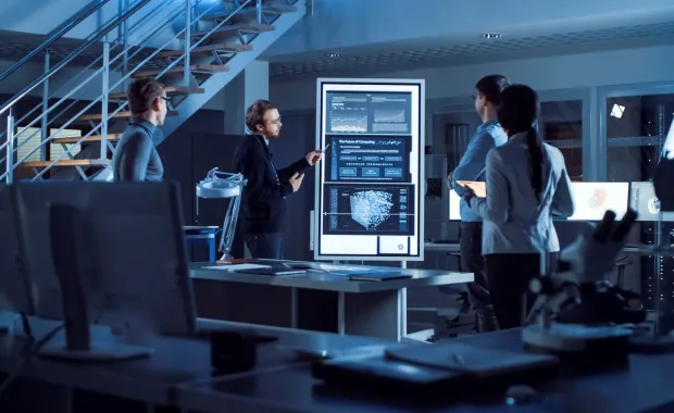 Project team standing meeting around a large digital display