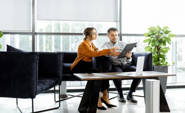 Zwei Personen sitzen auf einer Couch im Büro und besprechen gemeinsam ein Dokument