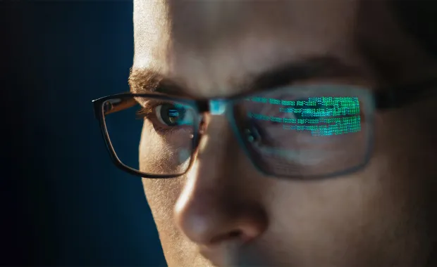 man with computer code reflected in eyeglasses