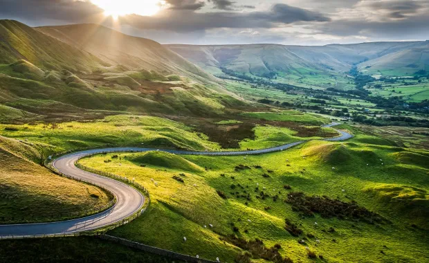 Road winding through rolling green hills on sunny day