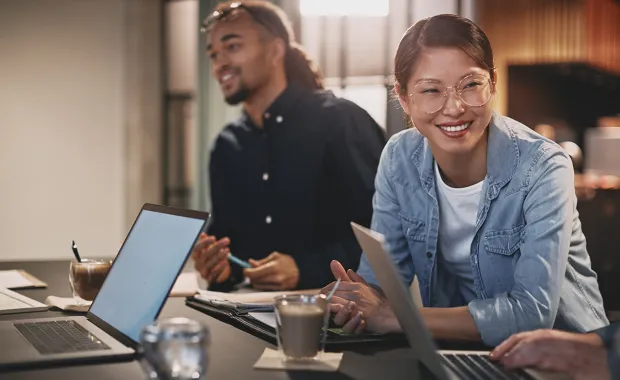 To personer smiler og jobber ved bord med bærbare PC-er og kaffe.