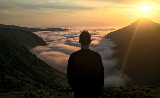 Kuvituskuvassa retkeilijä seisoo vuorella pilvirajan yläpuolella