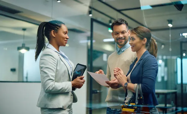 A financial advisor holding a tablet talks with two clients in a bright office