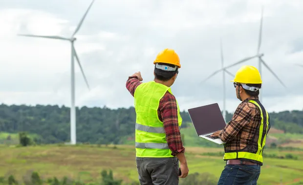 Två män tillsammans på ett fält inspekterar vindkraftverk
