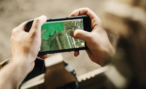 Soldier viewing geospatial imagery showing airstrip and surrounding terrain on a handheld device
