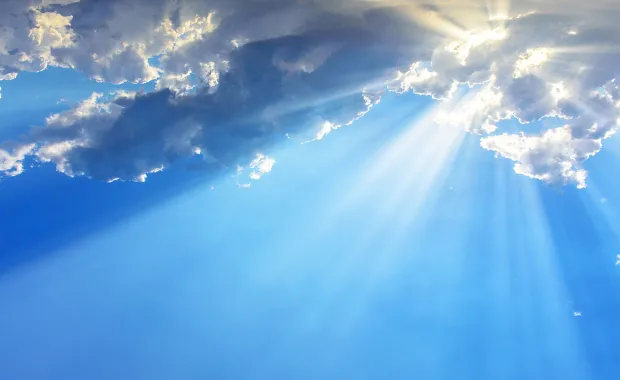 Solstrålar tränger fram genom moln på himlen och sprider ljus över en blå bakgrund.