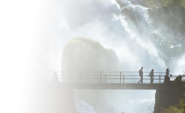 Tre personer går över en bro i naturen vid ett vattenfall