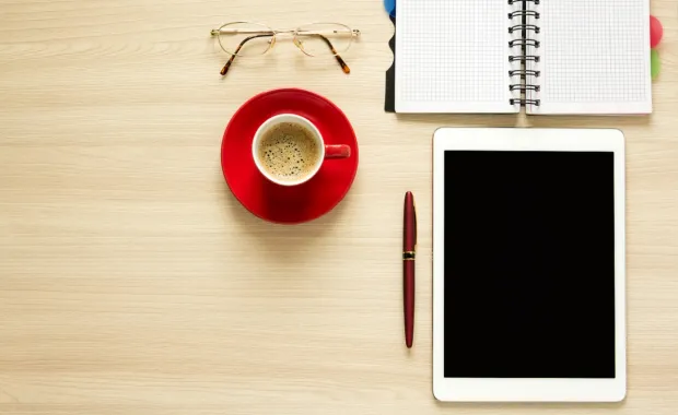 Tablet, coffee, note pad, pen, glasses on a desktop