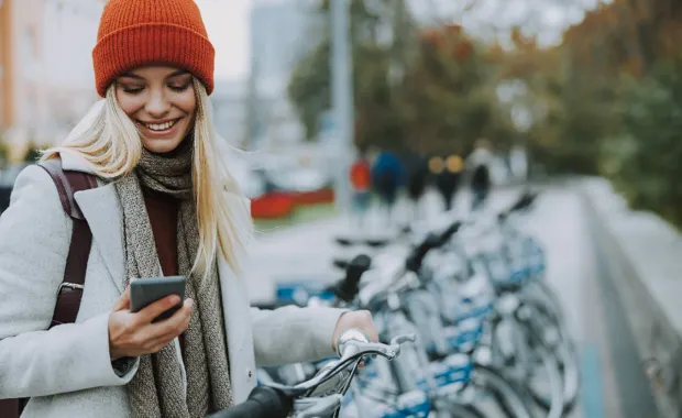 Kvinnlig student står vid cykelställ och scrollar på sin mobil