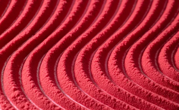Close-up of a textured red surface featuring a repeating pattern of curved, wave-like ridges.