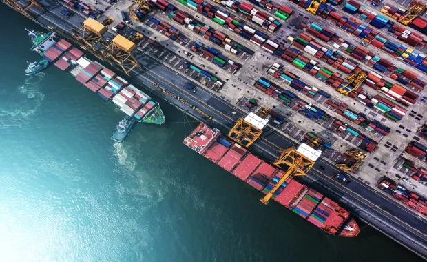 Draufsicht auf einen Hafen mit Frachtschiff und gestapelten Containern, Logistik und globaler Warenverkehr