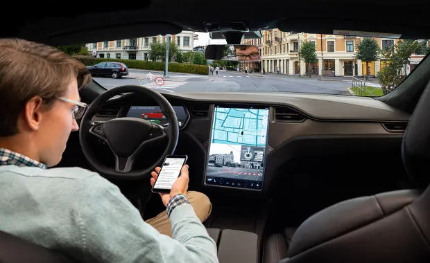 A man in driver seat of a car looking at a smartphone and car GPS