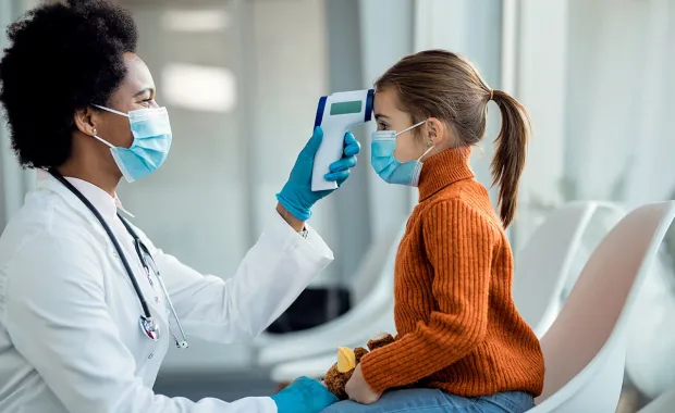 Läkare mäter temperaturen på en liten flicka i ett väntrum på kliniken