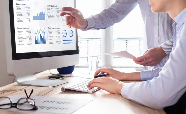 Two colleagues analyzing financial reports on a monitor