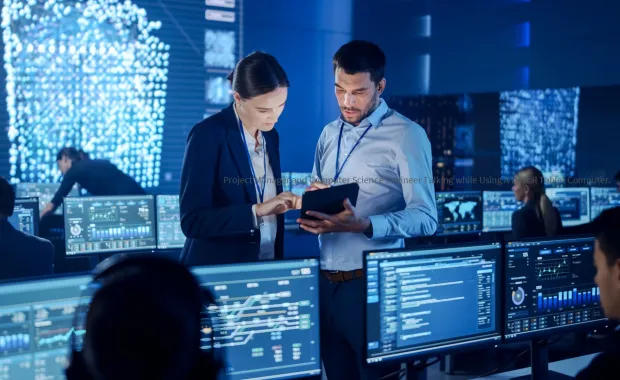 Two cybersecurity professionals discussion information on a tablet in a control room