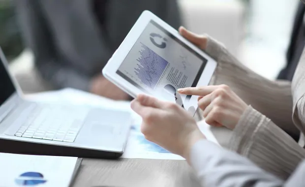 Close up of two people holding a digital tablet looking at a report with several graphs