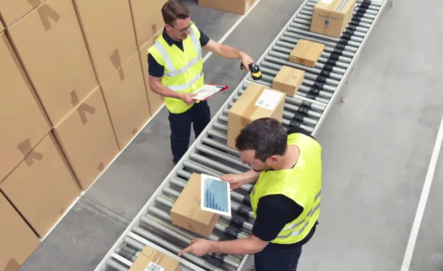 Two people scan packages on a conveyer belt using digital device