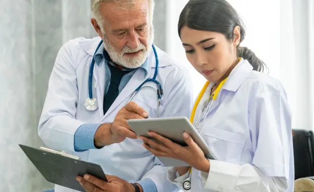 Two physicians reviewing a chart on a clipboard and tablet